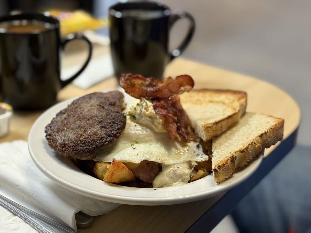 A breakfast plate with sausage, eggs, toast and two mugs of coffee